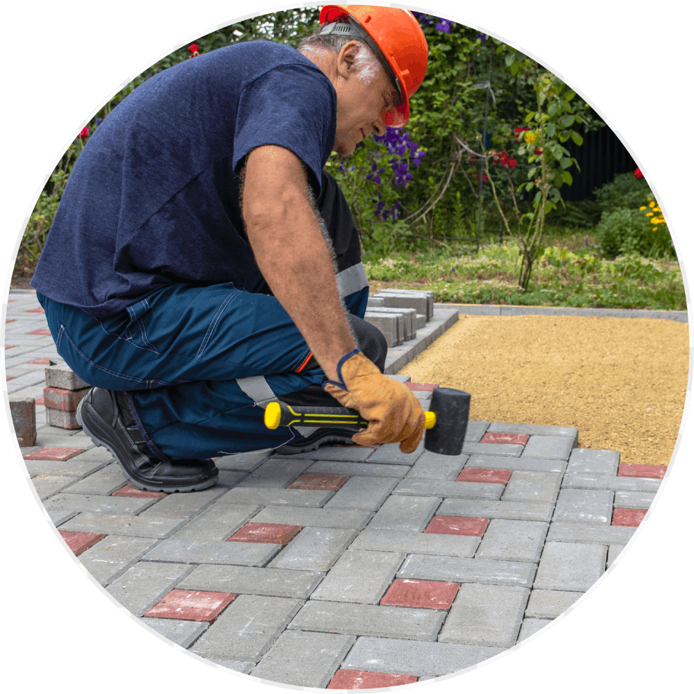 Worker installing interlocking paving stones outdoors.