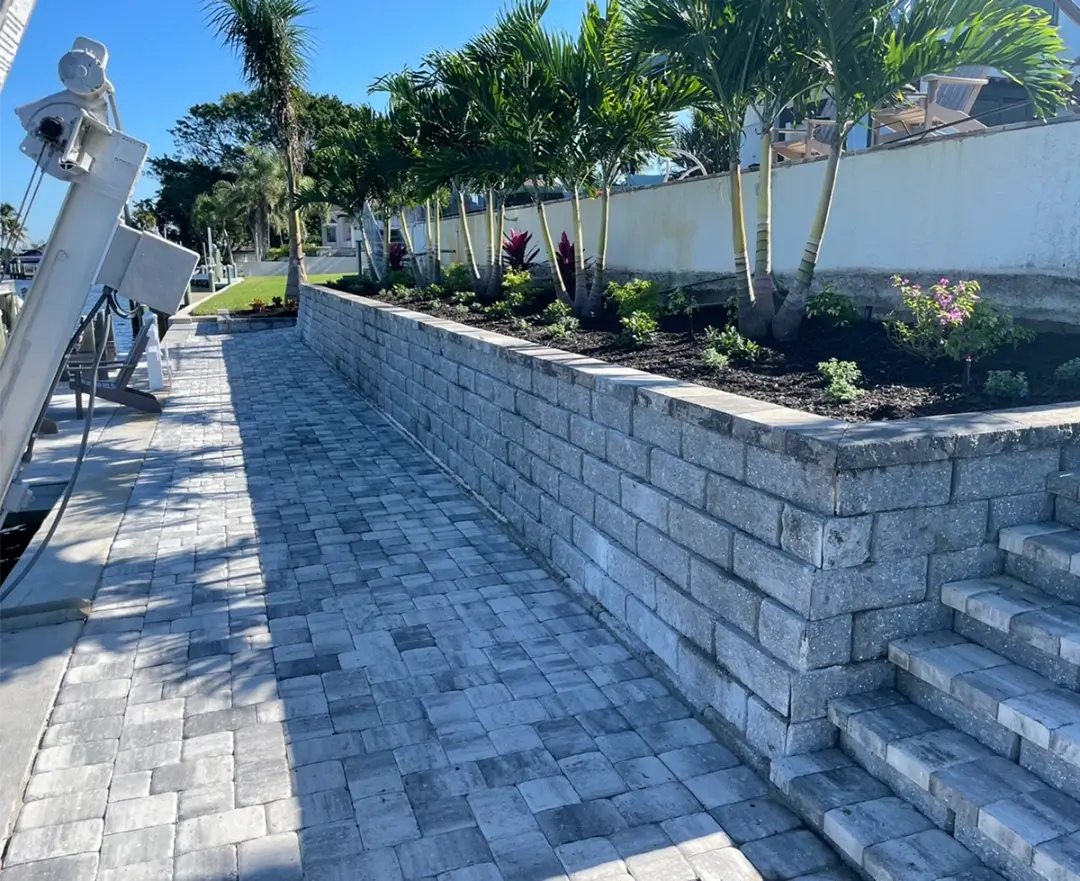 Brick retaining wall with landscaping and a paved walkway beside it.