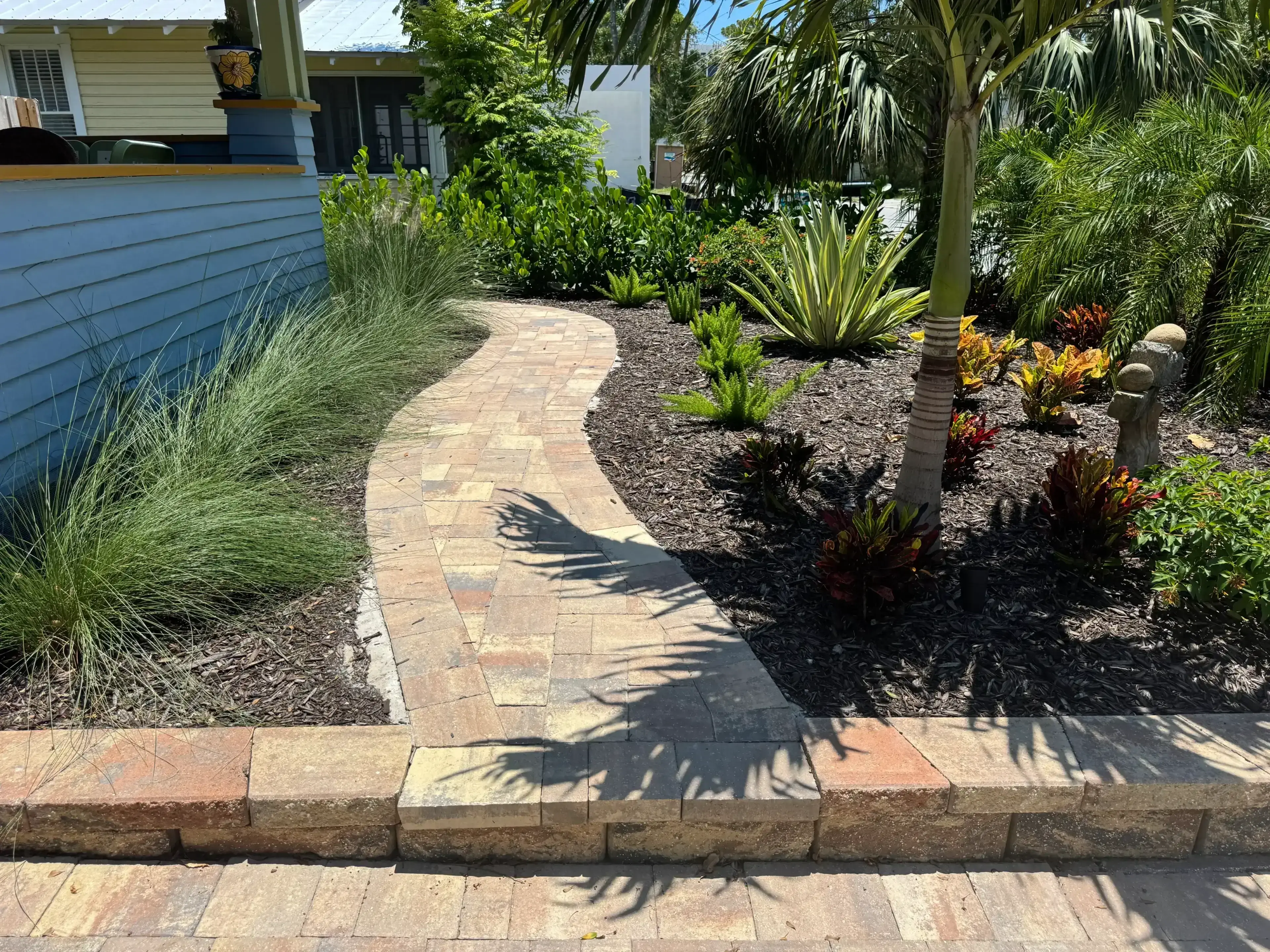 Curved brick pathway in a landscaped garden with tropical plants.