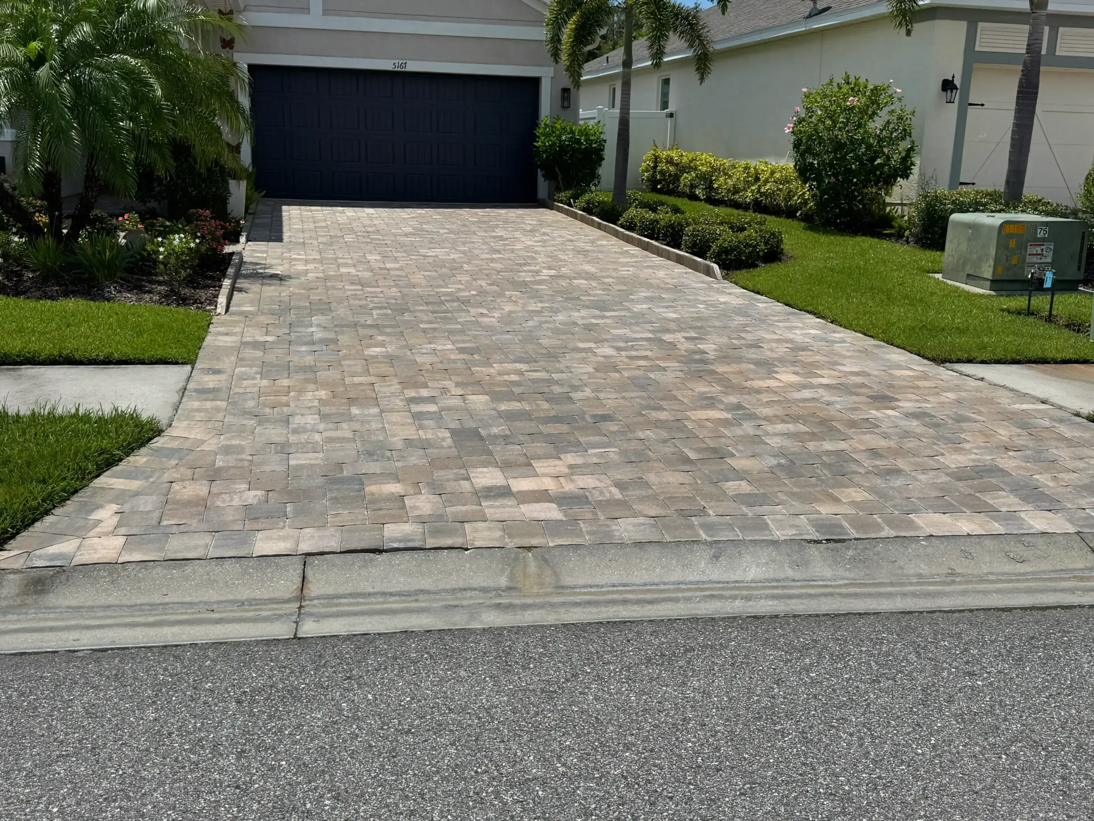 A clean, paved driveway leading to a modern garage with surrounding greenery.