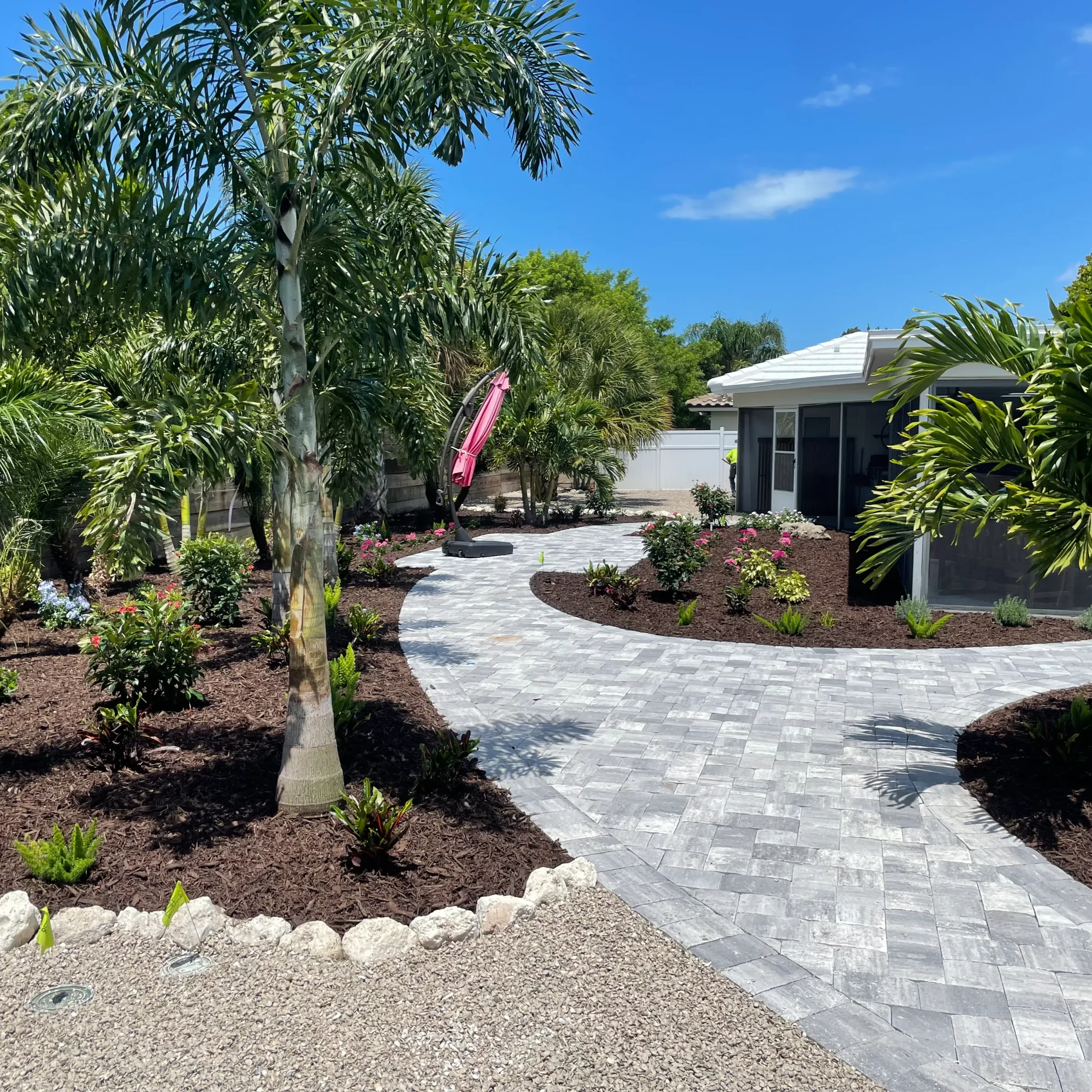 A winding stone path surrounded by palm trees and greenery under a clear blue sky.